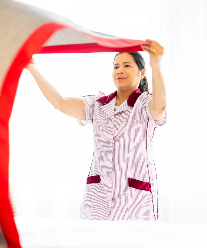 Housekeeping-Mitarbeiterin richtet die Bettdecke auf dem Hotelbett auf.